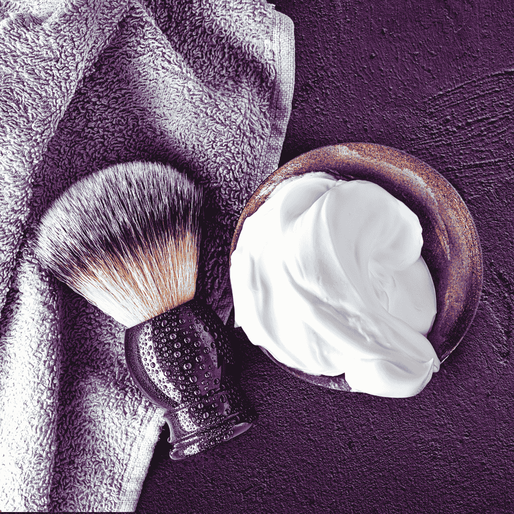 Shaving cream lather in a bowl. Shaving cream brush with black handle besides.