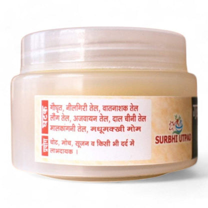 A jar of Surbhi Peedantak Ayurvedic Balm with a label detailing its ingredients (cow ghee, eucalyptus oil, clove oil, etc.) and uses for pain, swelling, and sprains.